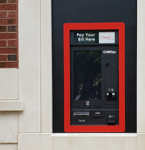 A red, through-the-wall, bill payment kiosk is installed on a brick wall.