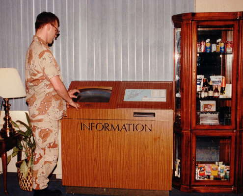 Explore the history of kiosks: A DoD servicemember uses one of DynaTouch's earliest information kiosks, featuring a classic wood panel exterior.