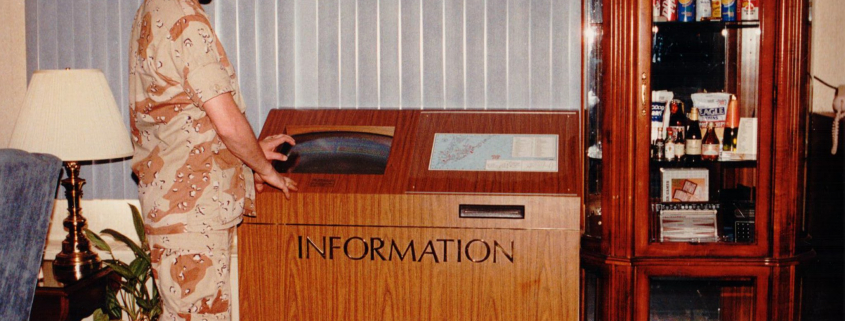 Explore the history of kiosks: A DoD servicemember uses one of DynaTouch's earliest information kiosks, featuring a classic wood panel exterior.